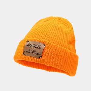 Detail of bright orange ribbed knit beanie featuring a brown textured letter patch
