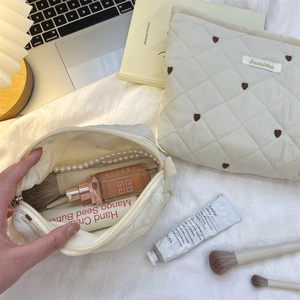 Quilted beige cosmetic bag with heart patterns and stationery brushes on white surface