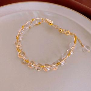 Macro detail of hand-woven gold wire bracelet with clear beads and adjustable chain clasp