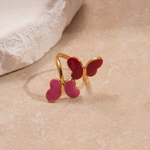 Detail of gold-plated butterfly ring with red and pink enamel on a stone surface
