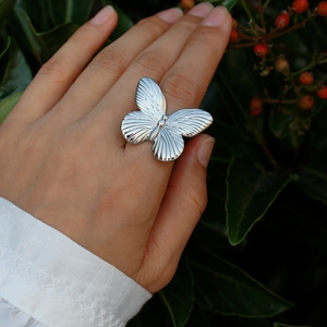 Elegant silver oversized 3D butterfly open ring on a model's finger with a natural botanical backdrop