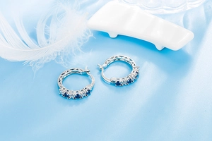 Close-up of S925 sterling silver hoop earrings with blue and clear crystals on silk fabric