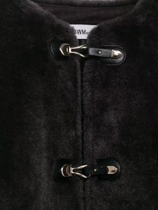Détail des boucles métalliques sur une veste en fausse fourrure sombre et cuir