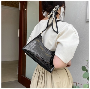Chic black crocodile embossed baguette bag worn over the shoulder by a model