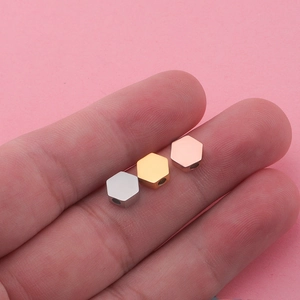 Polished hexagonal stainless steel beads in silver, gold, and rose gold on a fingertip