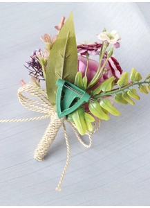 Detail of pink silk rose corsage with gold ribbon wrap and safety pin on light blue fabric