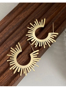 Detailed view of golden fan-shaped sunburst stud earrings on a dark wooden display tray