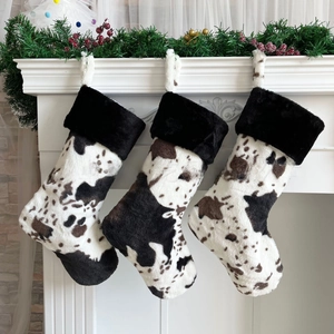 Three cow print Christmas stockings with plush black cuffs displayed by fireplace