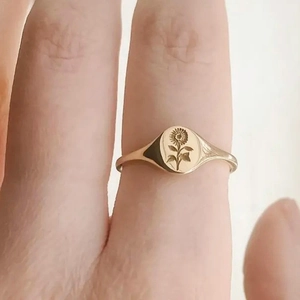 Detailed close-up of a gold signet ring with an intricate sunflower engraved on the face