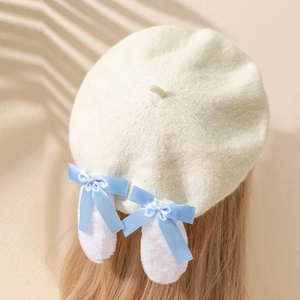 Détail d'un béret en tricot crème avec des nœuds en satin bleu et des oreilles de lapin