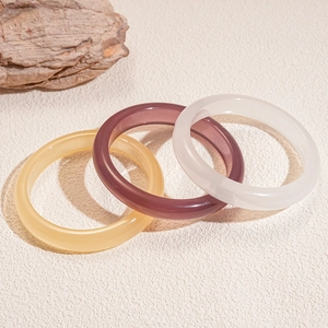 Three minimalist geometric resin bangles in yellow, purple, and white on a natural stone background