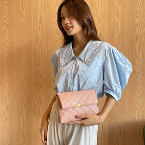 Pink quilted crossbody bag with gold chain strap shown on model against wooden background