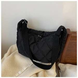 Detail of black quilted shoulder bag with dual zippers on warm beige cardigan
