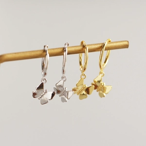 Detail view of silver and gold butterfly pendant hoop earrings on a metal display rod