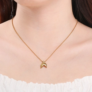Detail view of a gold hammered fish tail pendant necklace worn by a female model