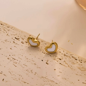Close-up of heart-shaped gold-plated earrings with white enamel on a stone texture