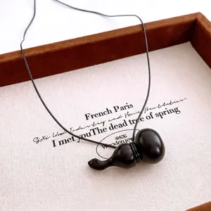 Collier avec pendentif gourde en bois vintage et cordon noir minimaliste sur plateau