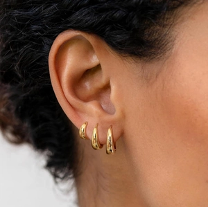 Three-piece set of 18K gold teardrop hoop earrings shown on ear in a layered style