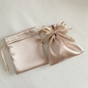 Close-up of champagne satin drawstring gift bags with silk ribbon bow on white texture