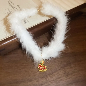 Detail of white plush choker with gold rocking horse pendant on vintage wood surface