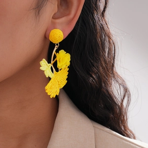 Detail of yellow raffia woven flower earring on a model for a chic summer vacation look