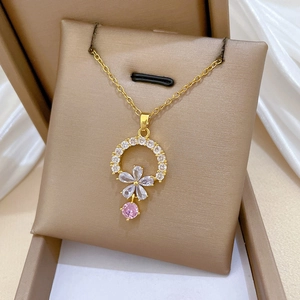 Macro view of gold flower necklace featuring pink zircon tassel on beige display card