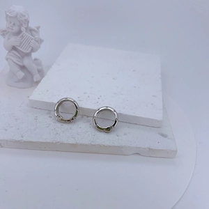 Silver round earrings with zircon pavé on white stone base with angel statue background