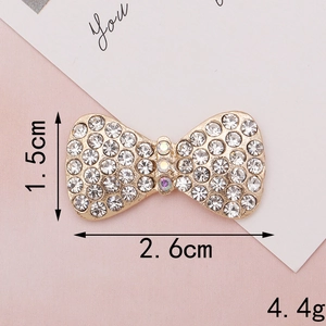 Macro shot showing dimensions 2.6cm x 1.5cm of a gold bow-knot with white rhinestones