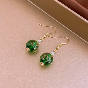 Macro shot of green glass bead earrings with gold leaf interior on a metallic tray