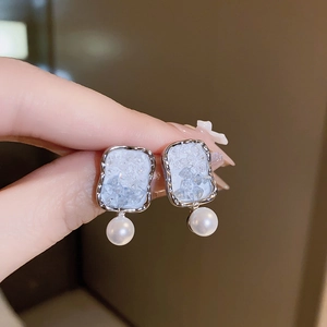 Detail of silver earrings featuring gradient crystal flowers and white pearl pendants