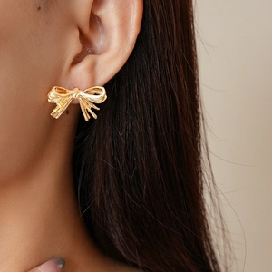 Macro shot of gold pleated bow earring with detailed silk-like metallic texture