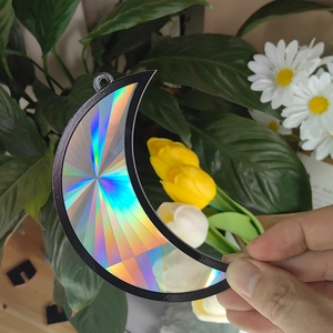 Detail of moon-shaped suncatcher with iridescent laser finish and black frame decoration