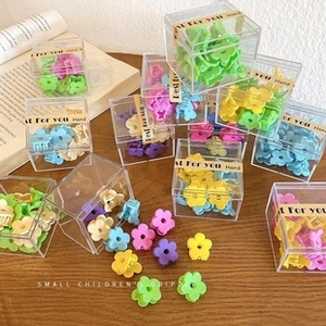 Flat lay of colorful flower-shaped hair claws in transparent boxes on wooden desk