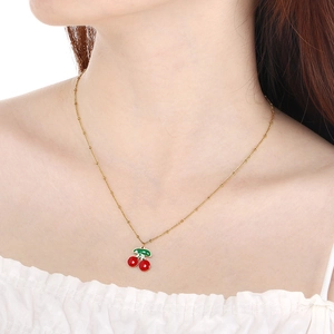 Collier doré avec pendentif cerise porté sur le cou pour un style estival chic