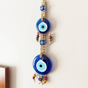 Handmade evil eye wall hanging with blue glass beads and macrame rope on white wall
