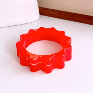 Vue détaillée d'un bracelet en acrylique rouge vif avec bords ondulés et texture