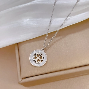 Macro shot of silver four-leaf clover necklace with shell inlay on white silk