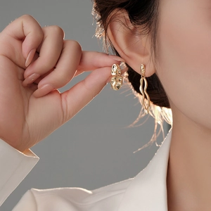 Close-up of asymmetrical gold lava textured earrings worn on ear showing metal luster