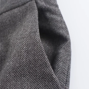 Close-up of grey herringbone fabric texture and pocket stitching on wide-leg trousers
