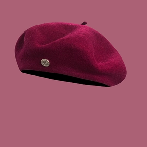 Detailed texture of a burgundy wool beret featuring a metallic decorative button on the side