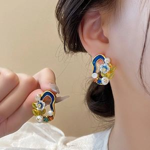 Detail of gold enamel floral earrings with blue and white petals and pearl accents