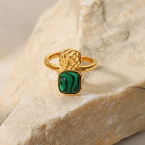 Macro shot of gold 18K ring with green stone set on textured stone background