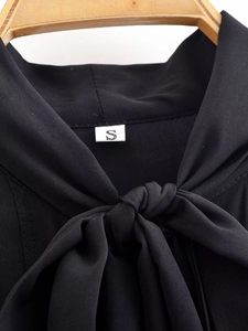 Detailed macro view of the black bow-tie neckline and size S label on a chiffon shirt