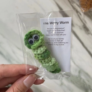 Macro shot of green crochet worry worm with healing poem card in a clear package