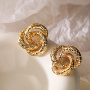 Elegantes pendientes de flores anudadas en oro con textura martillada en plato blanco