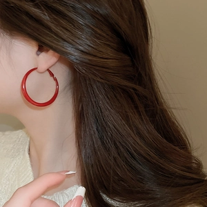 Close-up of model wearing vibrant red glossy hoop earrings with retro minimalist style