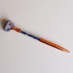 Detail of rose gold metal pen featuring raw lapis lazuli stone and blue crystal chips