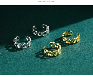 Detailed view of silver and gold heart-shaped ear cuffs on dark green background