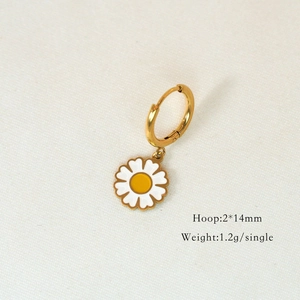 Detailed close-up of golden daisy enamel hoop earrings on light textured fabric background