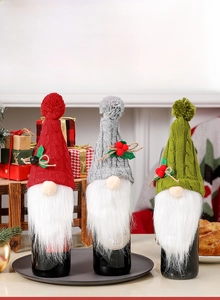 Close-up of three knitted Christmas gnome wine bottle covers in red, green and gray
